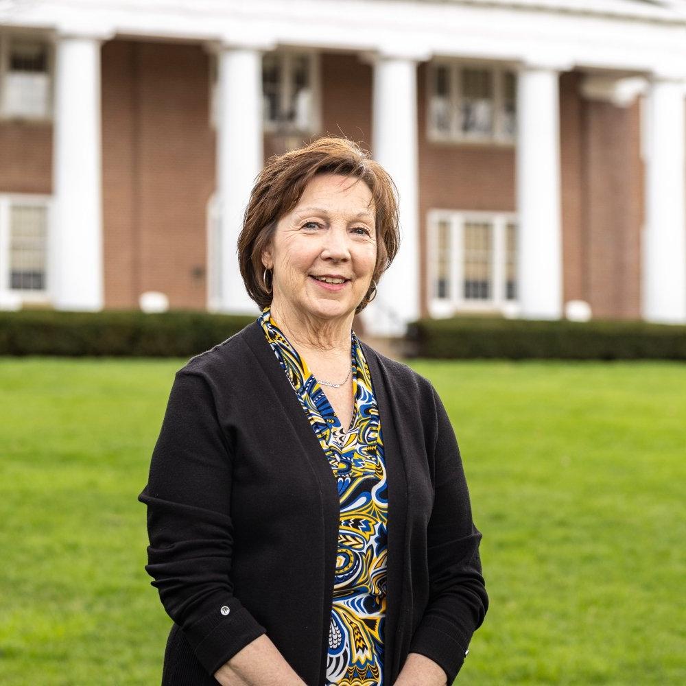 Lady with short brunette hair wearing multi colored patterned top with black cardigan standing in front of Old Centre