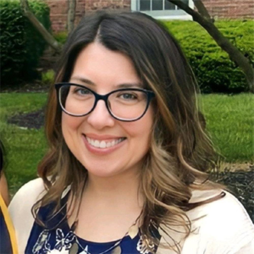 Lady with dark hair shoulder length wearing glasses and blue dress with white cardigan