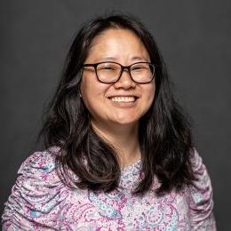 Jessica Leonard headshot - lady wearing glasses and pink paisley top in front of grey background