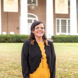 Lady with dark hair wearing black cardigan and gold top in front of old centre