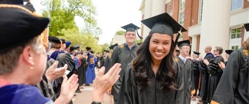 Students walking through lineup on graduation day in cap and gown being cheered on by professors