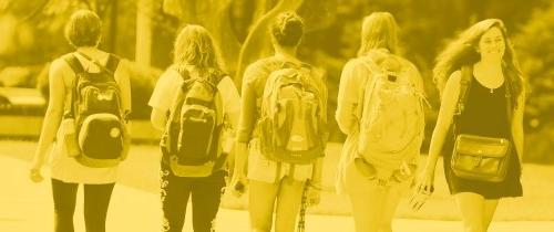 Student walking on campus wearing backpacks with gold tone